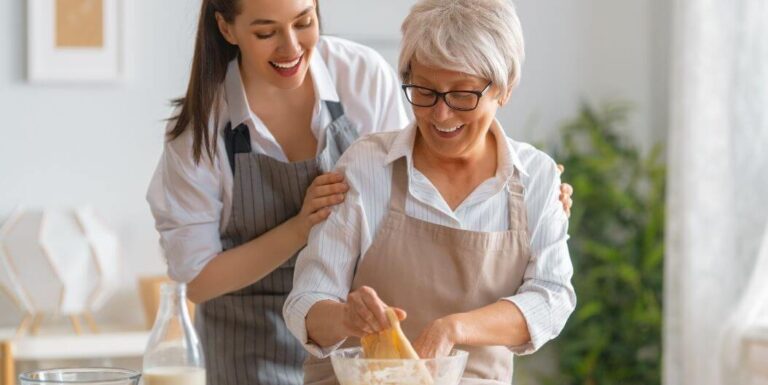 Female Nurse Helping a Senior Woman While Baking at Assisted Living Facility