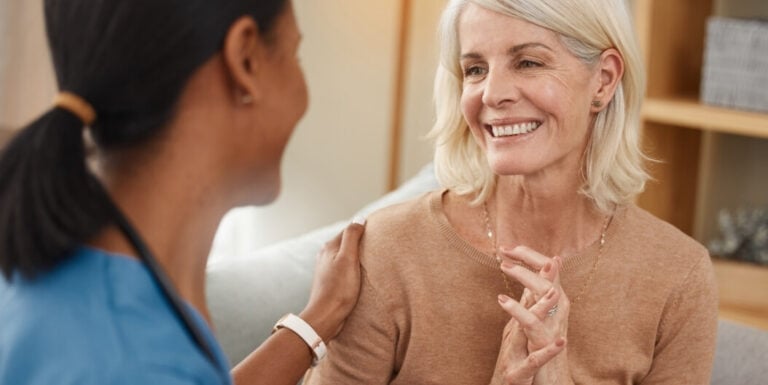 Female Nurse Comforting Elderly Woman During Conversation in Private Room Assisted Living Facility