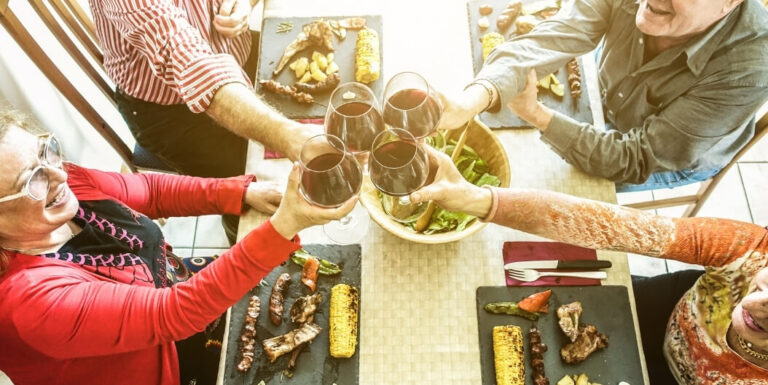 Elderly Friends Toasting Wine over a Protein-Rich Grilled Meal at Assisted Living Facility
