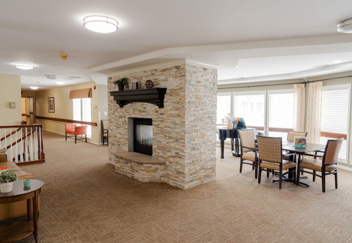 Open Common Area with Stone Fireplace and Dining Tables in Assisted Living Open Common Area with Stone Fireplace and Dining Tables in Assisted Living